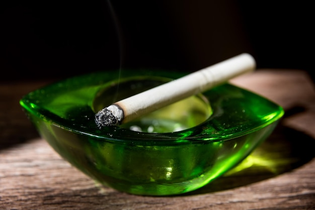 Cigarette resting on green ashtray with black background nicotine addictions