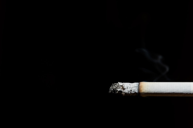 Cigarette with ash peeking out from the right on black background drugs consumption addiction