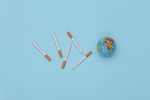 Cigarettes and globe on blue background. Top view