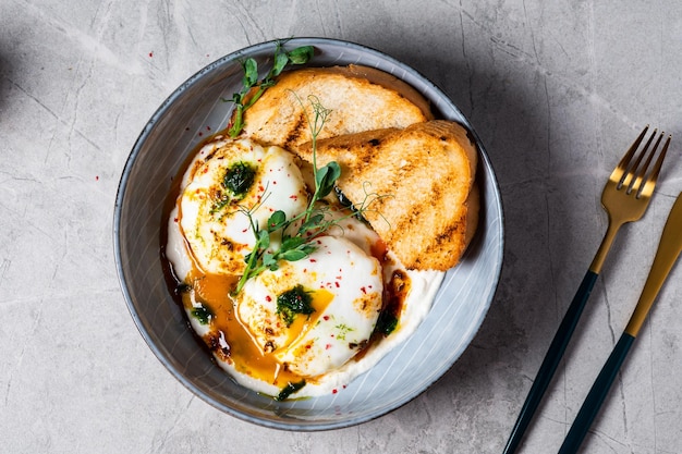 Cilbir or Turkish Eggs dish served as mezze poached eggs topped over herbed greek yogurt then drizzled with hot spiced paprika olive oil Turkish breakfast in a grey bowl on marble background