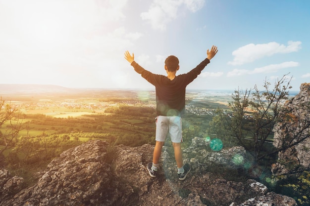 Cild standing on of stump in summer mountains at sunset and enjoying view of nature