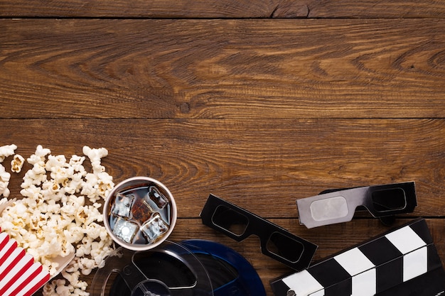 Photo cinema background, top view. clapperboard, popcorn, soda and 3d glasses on wooden table, copy space. movie goers accessories, cinematography concept