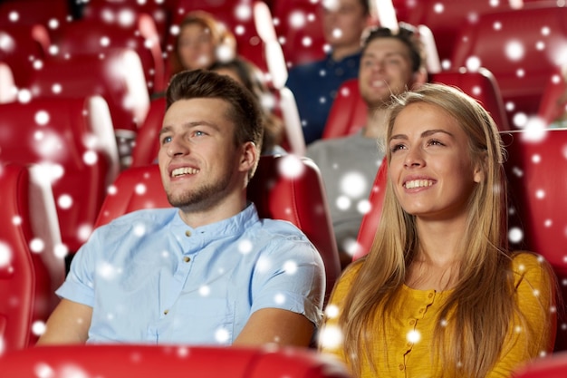 cinema, entertainment and people concept - happy friends or couple watching movie in theater over snowflakes