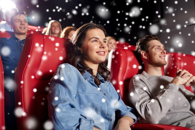 cinema, entertainment and people concept - happy friends watching movie in theater with snowflakes