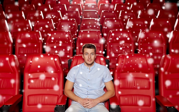 cinema, entertainment and people concept - happy young man watching movie alone in empty theater auditorium with snowflakes