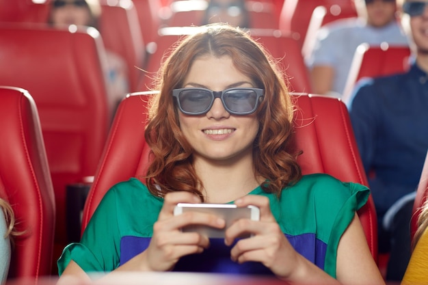 cinema, technology, entertainment and people concept - happy woman with 3d glasses and smartphone reading message in movie theater