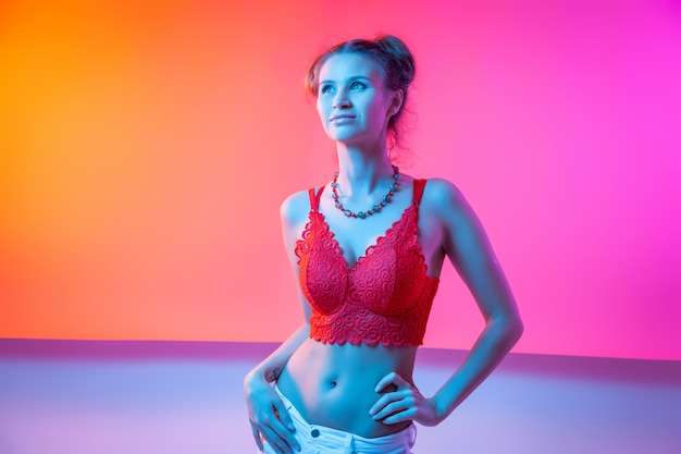 Cinematic night portrait of woman in neon. High Fashion model girl in colorful bright neon lights posing, portrait of beautiful woman in top and jeans. 