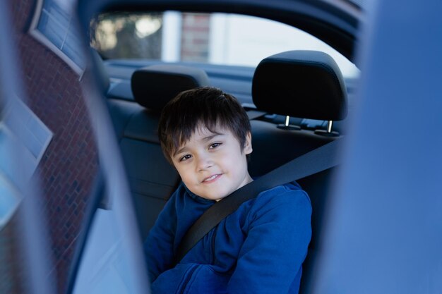 Cinematic portrait boy siting in safety car seat looking at camera with smiling faceChild sitting in the back passenger seat with a safety belt School kid traveling to school by carBack to school