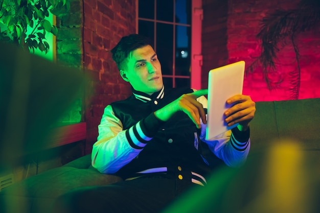 Cinematic portrait of handsome young man using devices, gadgets in neon lighted interior.