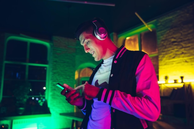 Cinematic portrait of handsome young man using devices gadgets in neon lighted interior