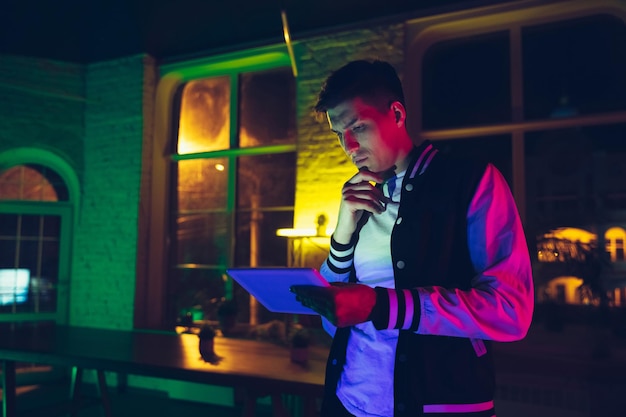 Cinematic portrait of handsome young man using devices, gadgets in neon lighted interior.