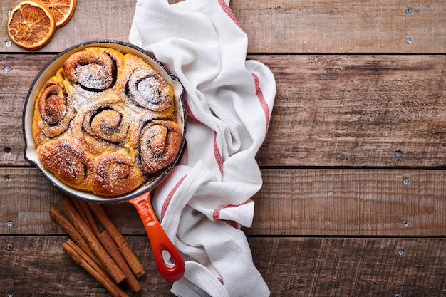 Cinnabon cinnamon rolls buns with pumpkin, nut, caramel and sugar cream iced on rustic wooden background table. Top view. Sweet Homemade Pastry christmas baking. Kanelbule - swedish dessert.