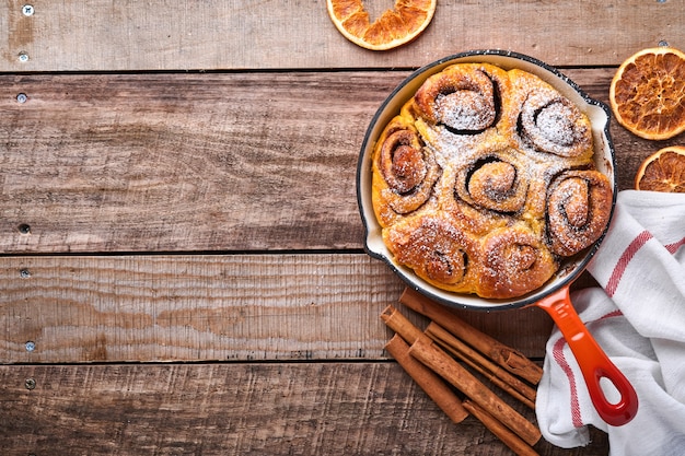 Cinnabon cinnamon rolls buns with pumpkin, nut, caramel and sugar cream iced on rustic wooden background table. Top view. Sweet Homemade Pastry christmas baking. Kanelbule - swedish dessert.