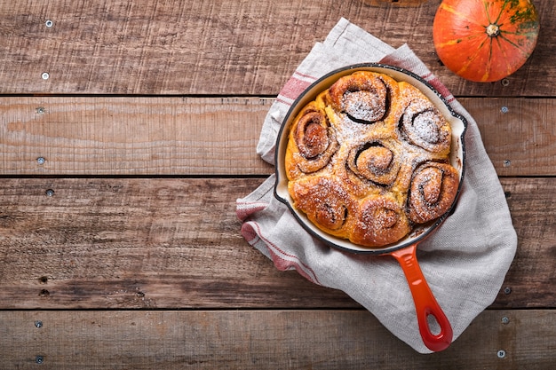 Cinnabon cinnamon rolls buns with pumpkin, nut, caramel and sugar cream iced on rustic wooden background table. Top view. Sweet Homemade Pastry christmas baking. Kanelbule - swedish dessert.