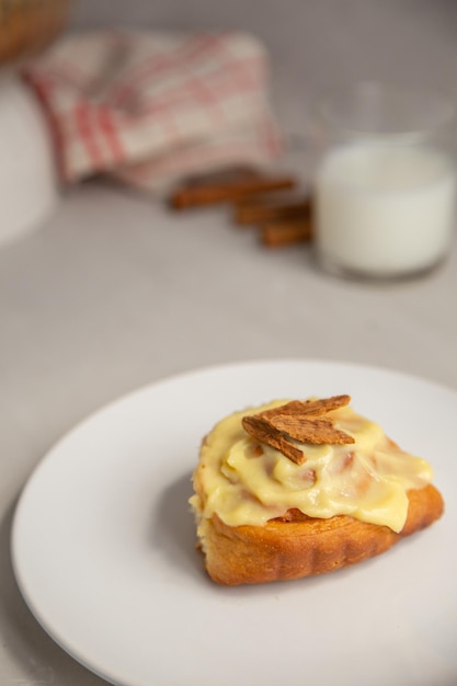 cinnamon bun with icing and cinnamon sticks with a glass of milk on a light gray background