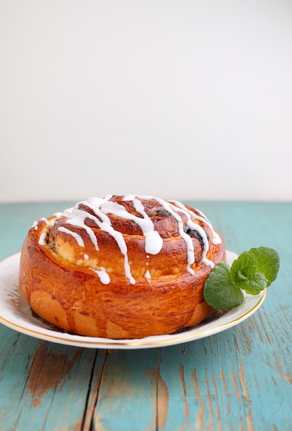 Cinnamon and icing bun decorated with mint in a plate on a light blue wooden background