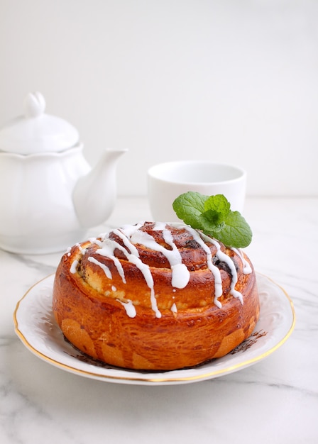 Cinnamon and icing bun decorated with mint in a plate on marble background