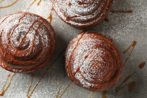 Cinnamon rolls with caramel and powdered sugar on grey table 