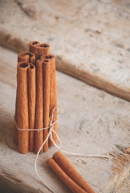 Cinnamon sticks tied in one bunch next to one cinnamon stick on a wooden surface.