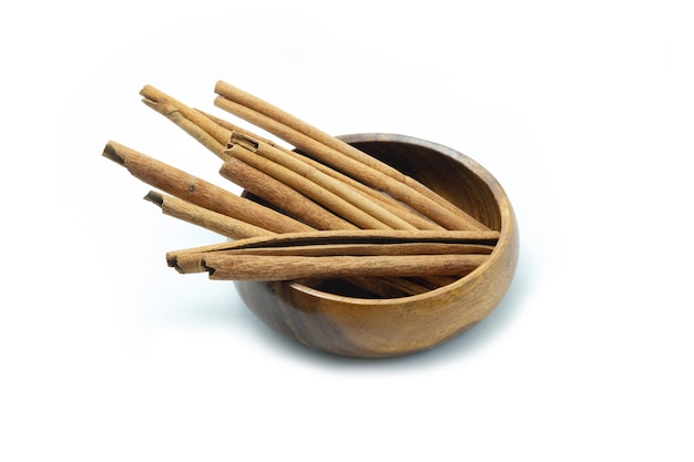 Cinnamon sticks in wooden bowl on white background.