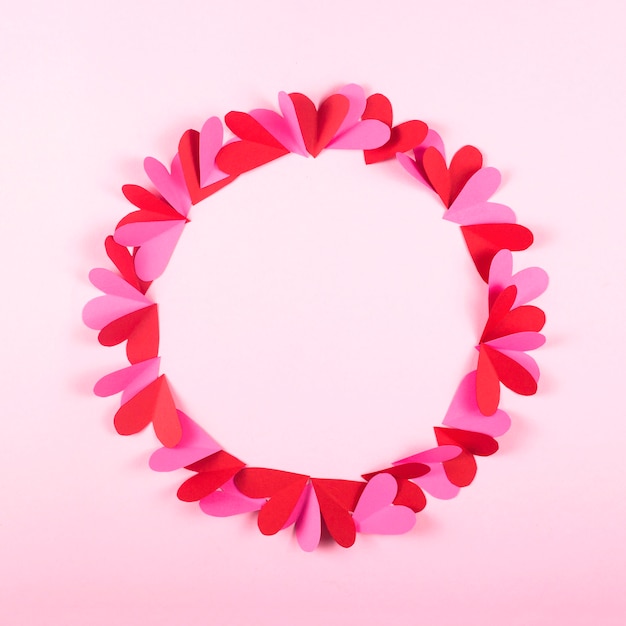 Circle of paper hearts on a pink background for Valentine's Day.