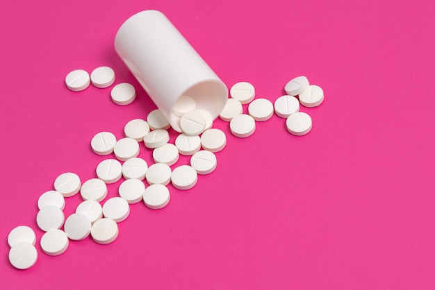 Circle pills tablets spilling out of a white plastic medicine bottle