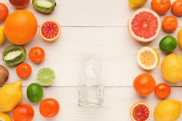 Citrus background. Assorted fruits and empty glass for fresh juice on white wooden planks. Healthy lifestyle, natural vitamins concept, top view, copy space, blogger flat lay