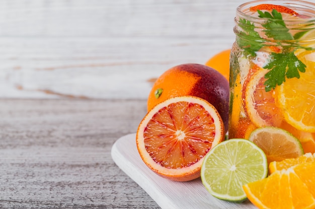 Citrus fruit and herbs water for detox or dieting in glass bottles on wooden board