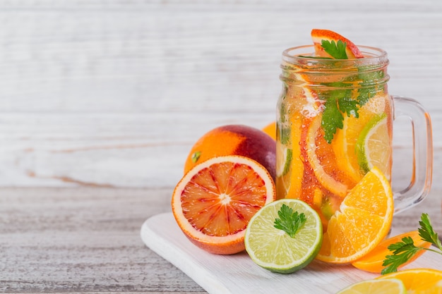 Citrus fruit and herbs water for detox or dieting in glass bottles on wooden board