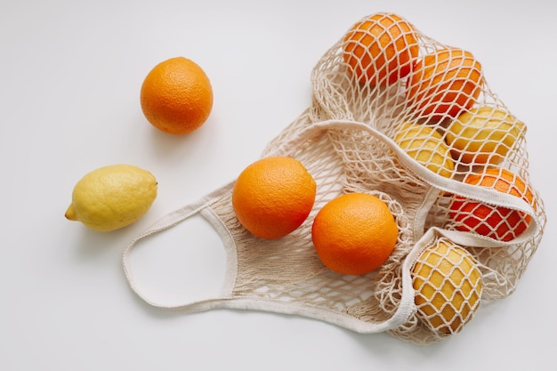 Citrus fruits in reusable bag on white background flat lay top view copy space