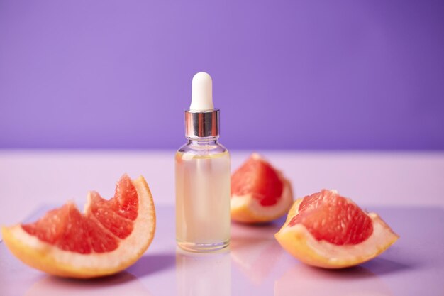 Citrus or grapefruit essential oil in glass bottle with fresh grapefruit on trendy purple background Spa and skincare product