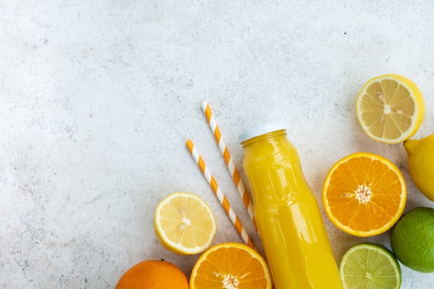 Citrus juice in glass bottle with oranges and lemons on light marble background