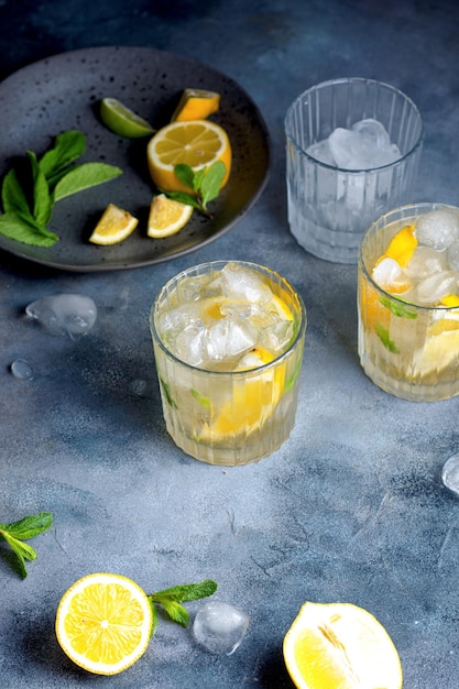 Citrus lemonade with mint and lemon in the glass with ice cubes fresh ingredients lemon and mint on gray ceramic plate