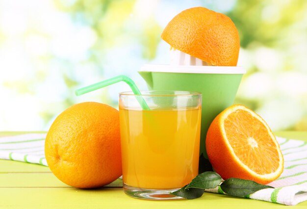 Citrus press glass of juice and ripe oranges on white wooden table