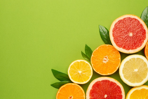 Citruses fruits on green background with copyspace, fruit flatlay, summer minimal composition with grapefruit, lemon, mandarin and orange