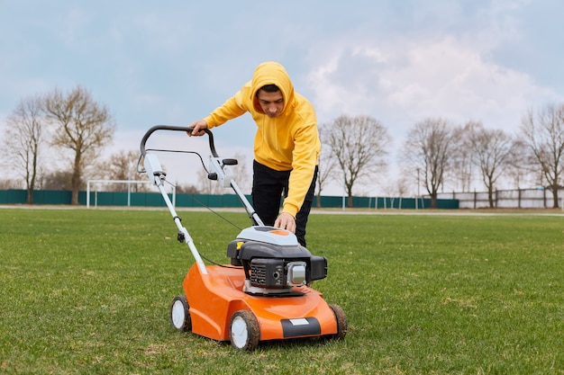 City landscaper man gardener worker cutting grass around planted with lawn mower