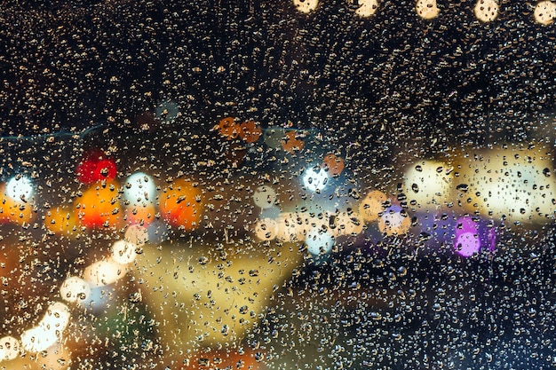 City lights of the night during the rain behind a glass covered with drops of water.