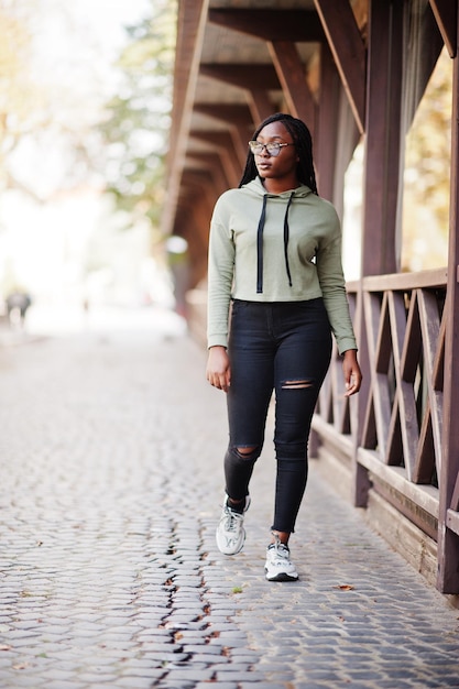 City portrait of positive young dark skinned female wearing green hoody and eyeglasses