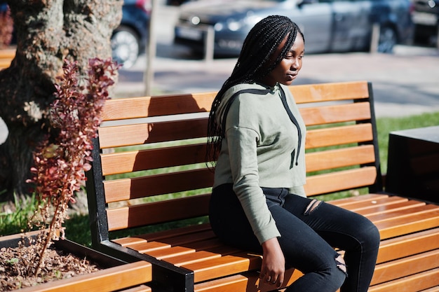 City portrait of positive young dark skinned female wearing green hoody sitting on bench