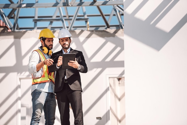 Civil engineer and construction worker manager holding digital tablet and blueprints talking and planing about construction site Cooperation teamwork concept