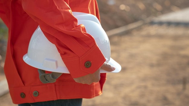 A civil engineer in coverall uniform is holding a with safety hardhat helmet on construction site ba