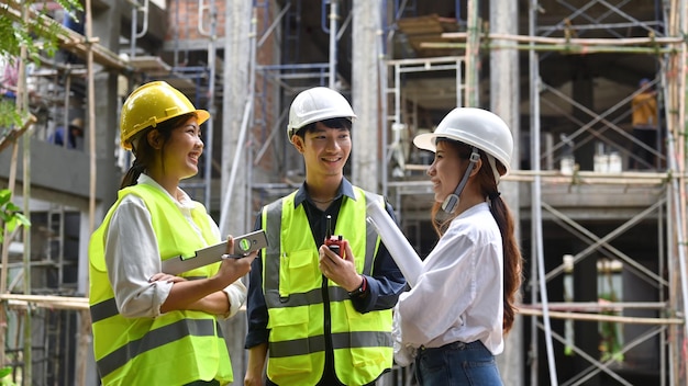 Civil engineer team wearing yellow vests discussing the construction process together on the open building site near the crane