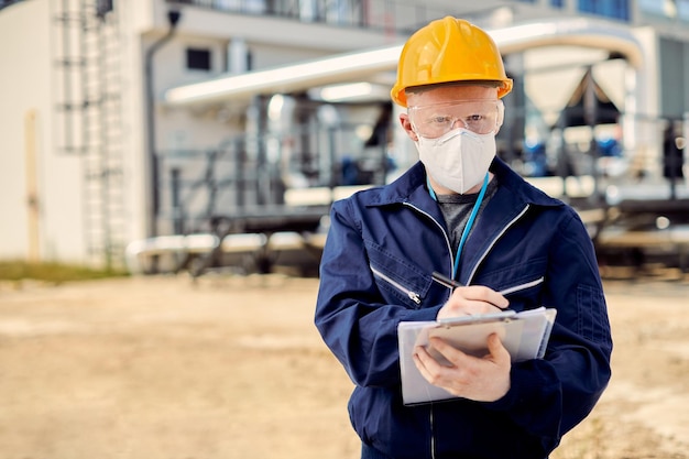 Civil engineer with protective face mask taking notes while working at construction site