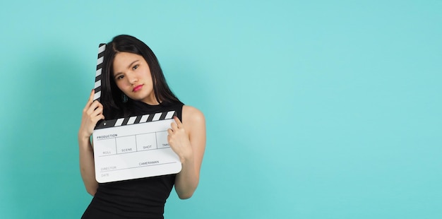 Clapper board or movie clapperboard in woman hand with black color.it use in video production ,film, cinema industry on green or Tiffany Blue background.she wear black dress