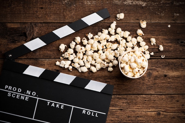 Clapper board and popcorn on wooden background, top view close up