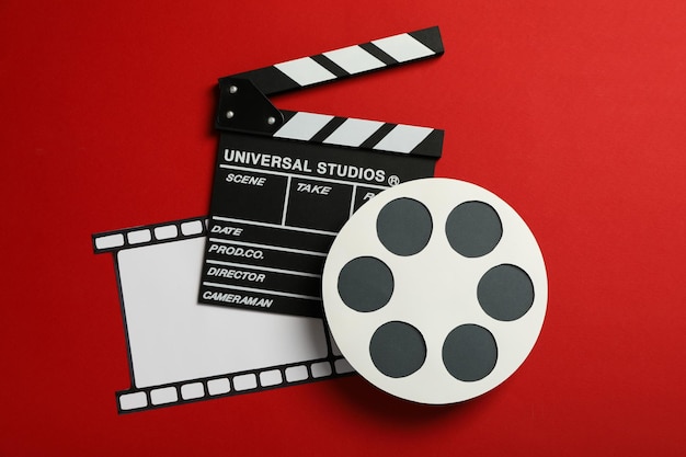 Clapperboard paper reel and film on red background top view