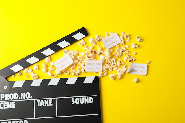 clapperboard, popcorn and tickets on yellow background