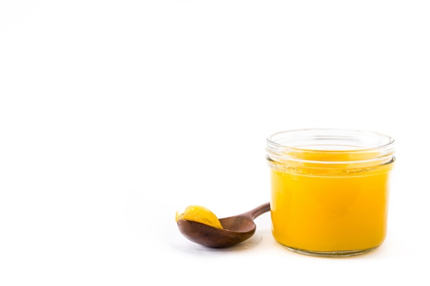 Clarified butter in jar and wooden spoon isolated on white background