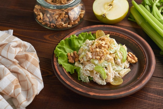 Classic american waldorf salad made of apples celery walnuts grapes mayonnaise whipped cream white plate brown background