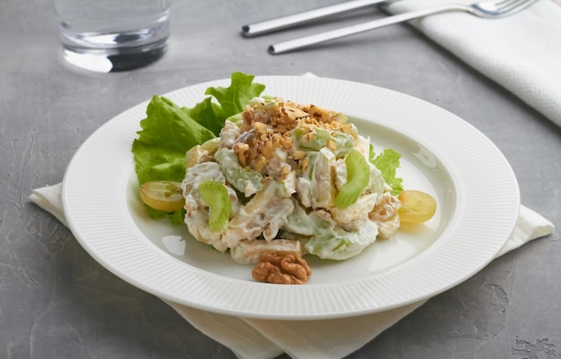 Classic american waldorf salad made of apples celery walnuts grapes mayonnaise whipped cream white plate grey background